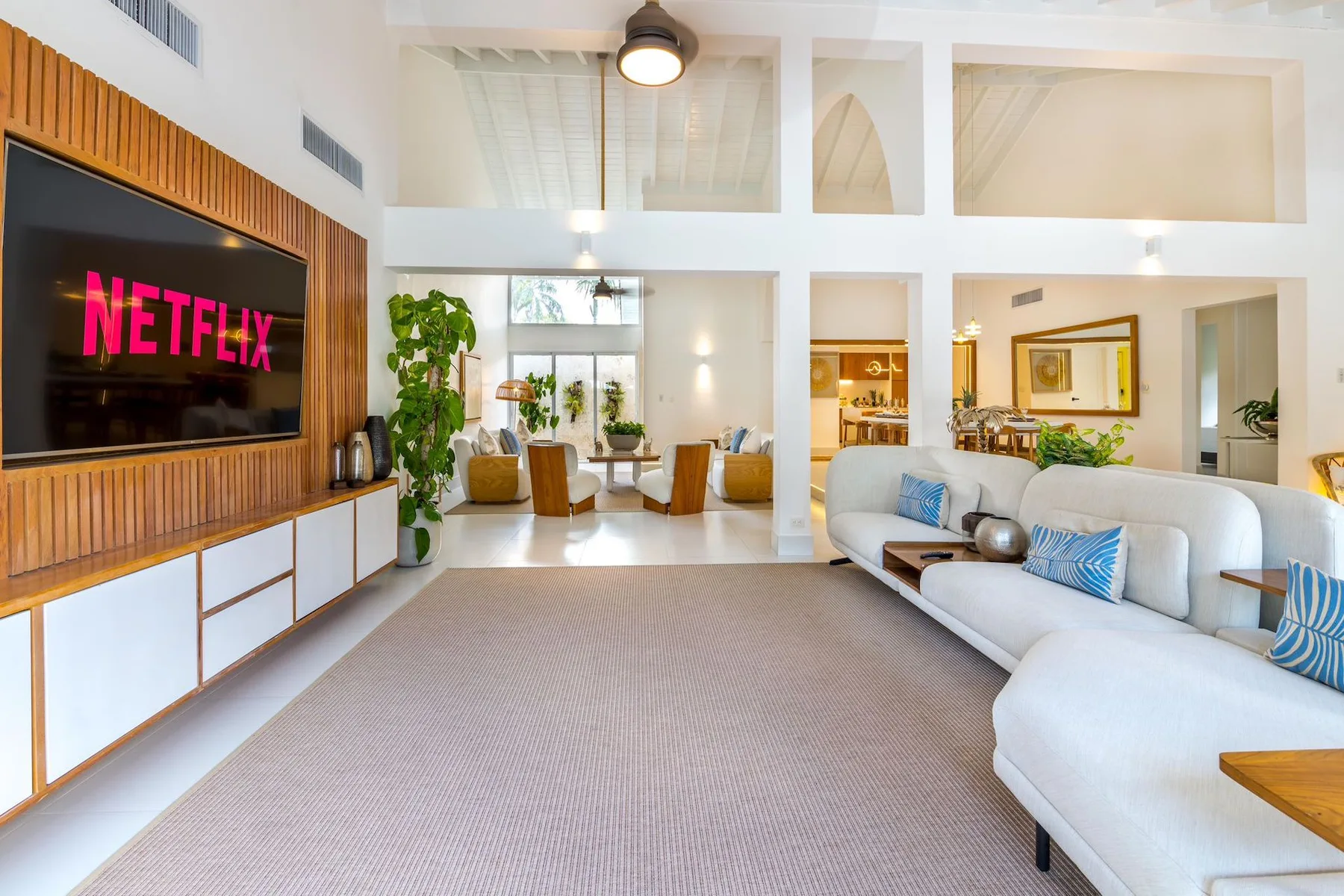 A bright living room with a large television and white seating.