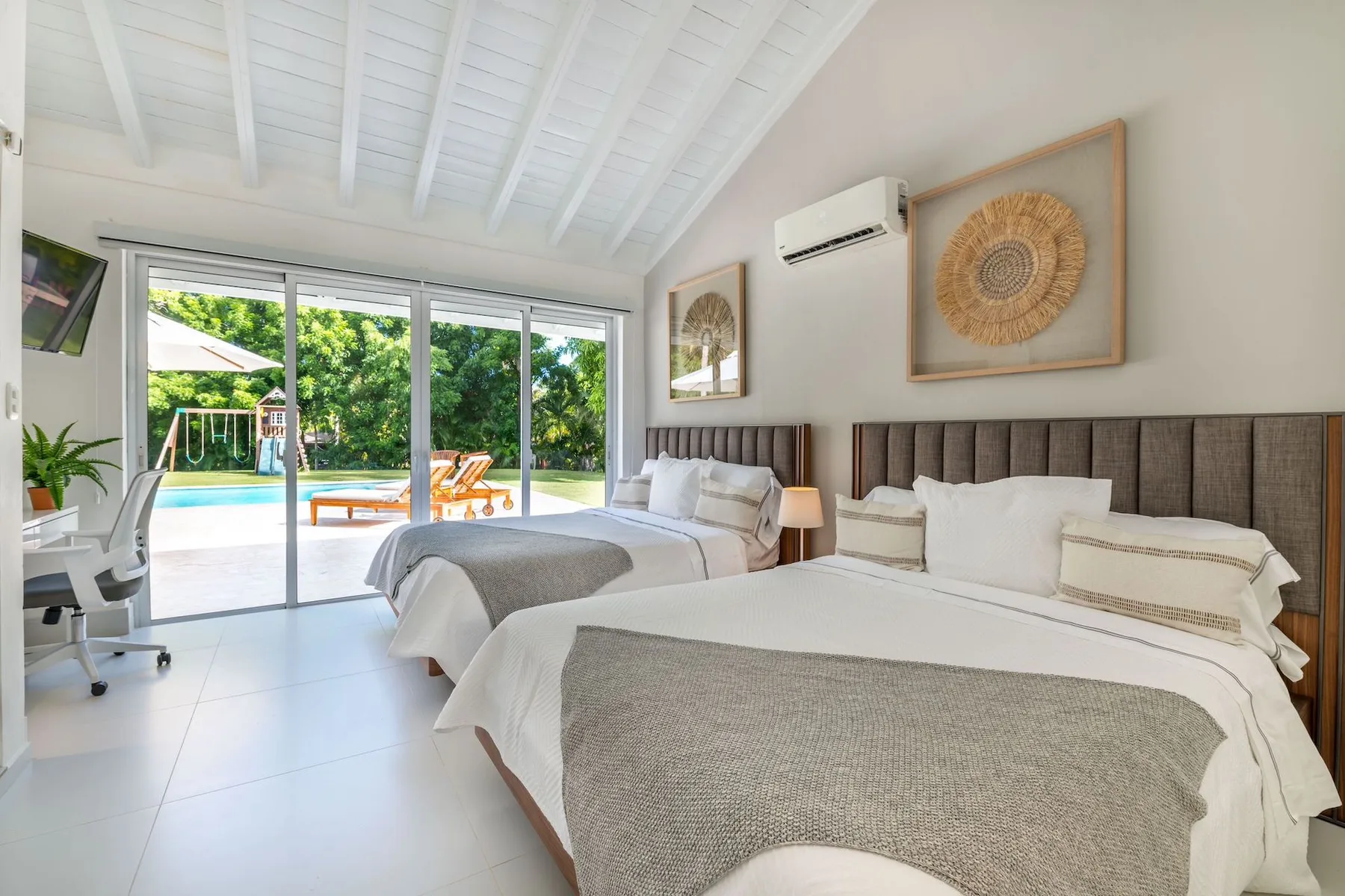 A bright bedroom with two beds beside large windows overlooking a garden.
