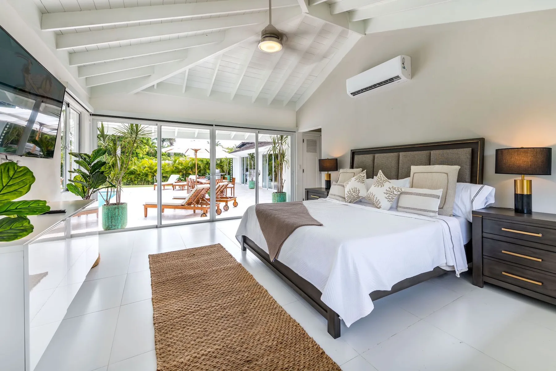 A bright bedroom with a large bed, bedside tables, and glass doors opening onto greenery.