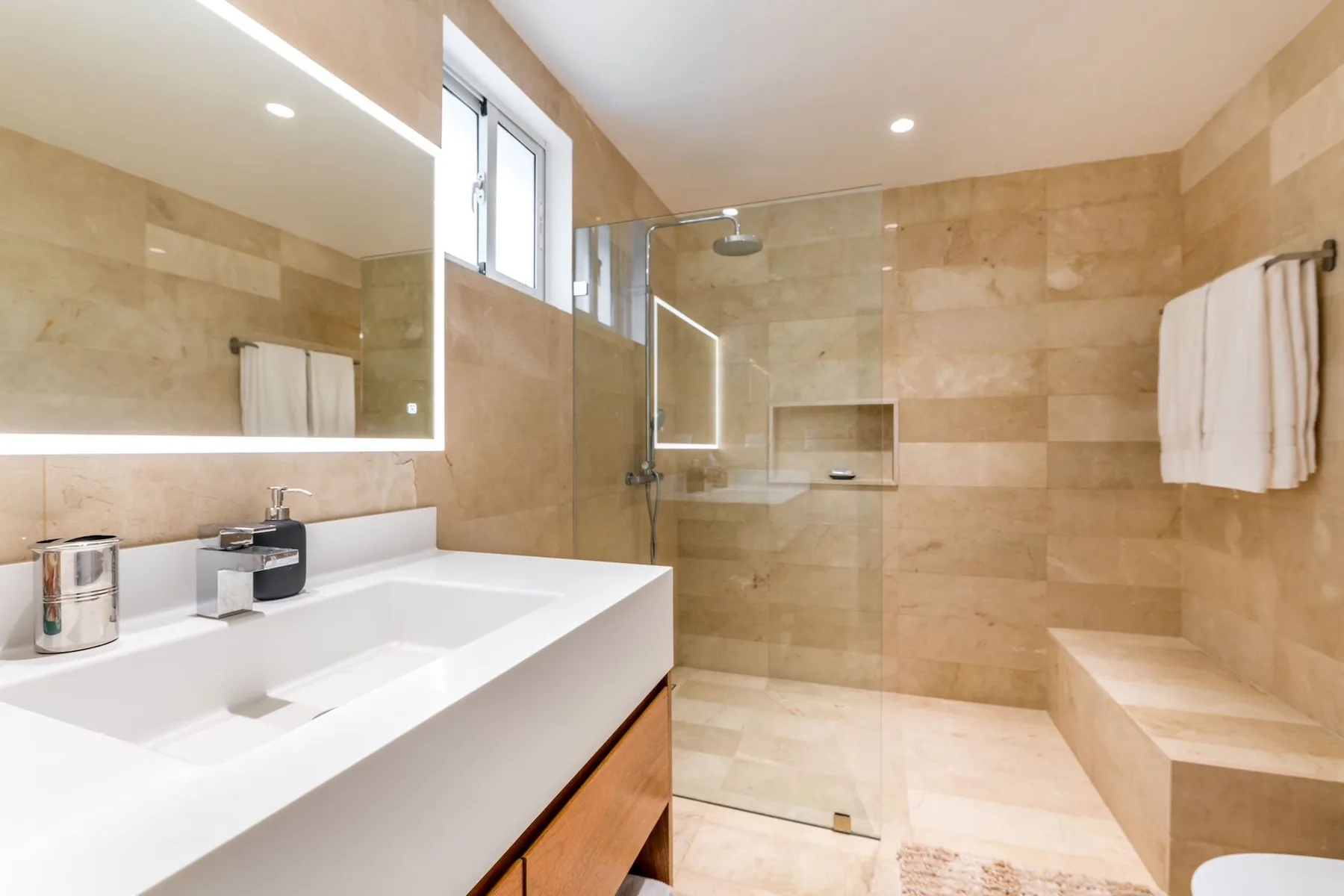 A bright bathroom with a wide vanity, a glass shower, and a built-in bench.