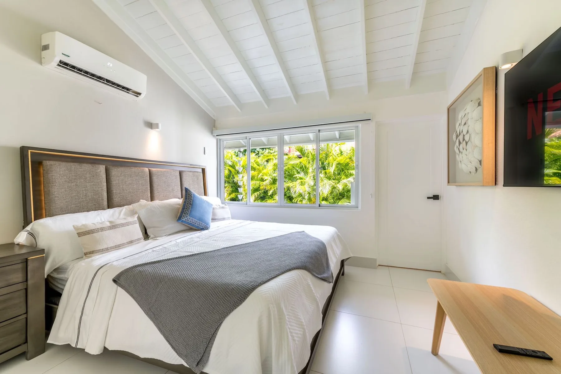 A bedroom with a large bed and a window overlooking green foliage.