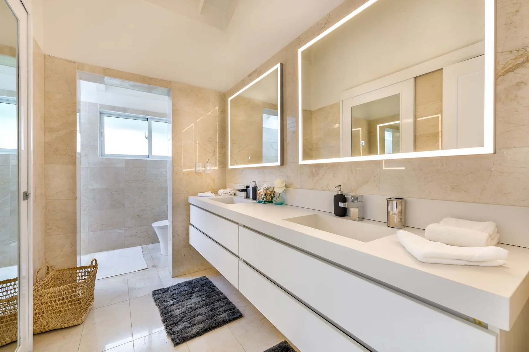A bright bathroom with a long vanity, sinks, and illuminated mirrors.