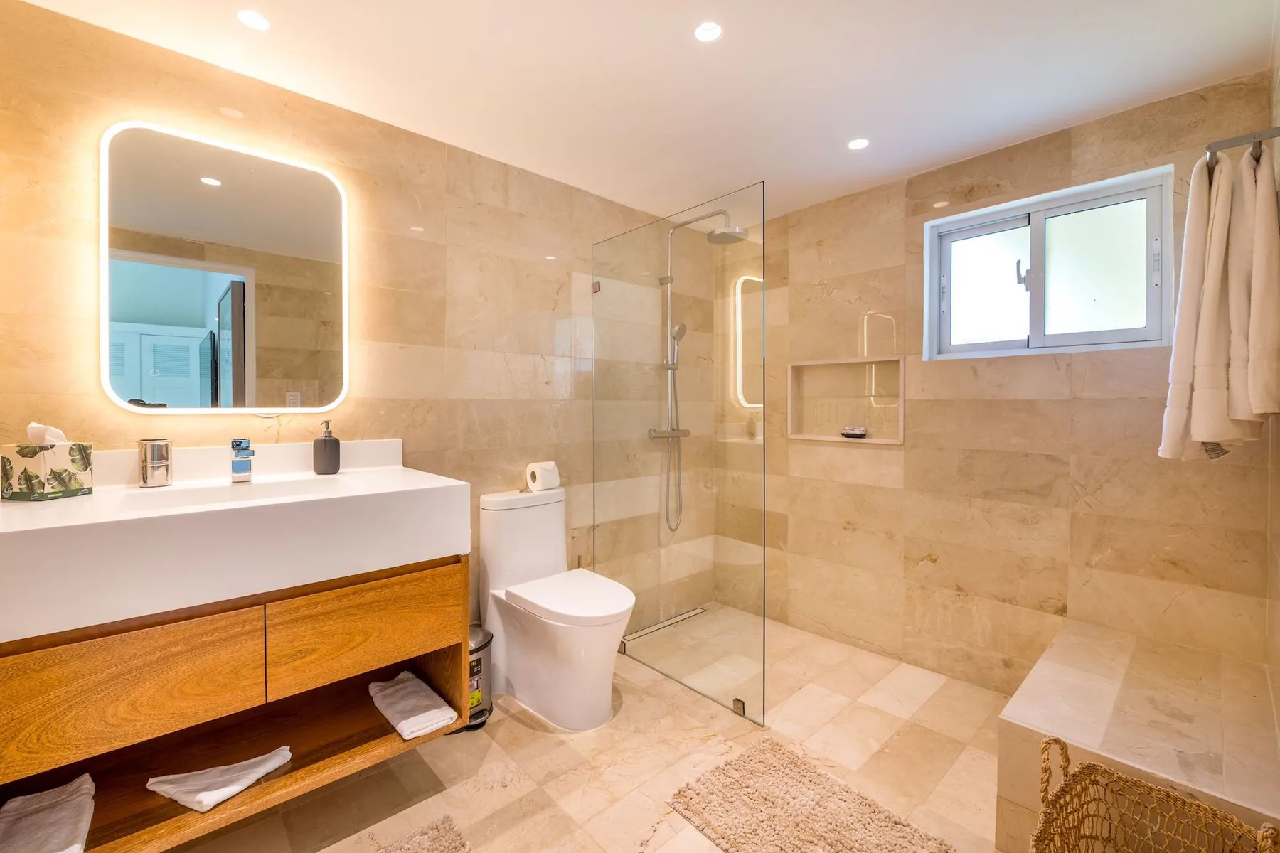 A bright bathroom with a vanity, toilet, and glass shower.