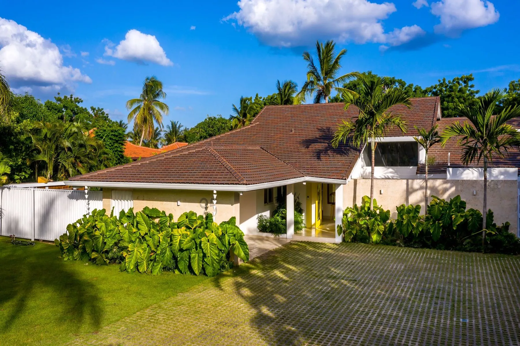 A tropical house with a tiled roof, palm trees, and a paved driveway.