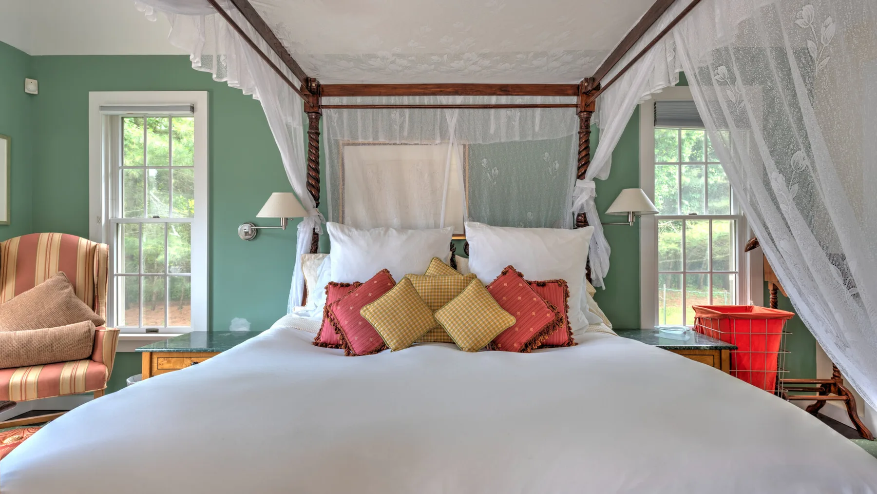Un dormitorio con una gran cama con dosel, cojines de colores y ventanas a ambos lados.