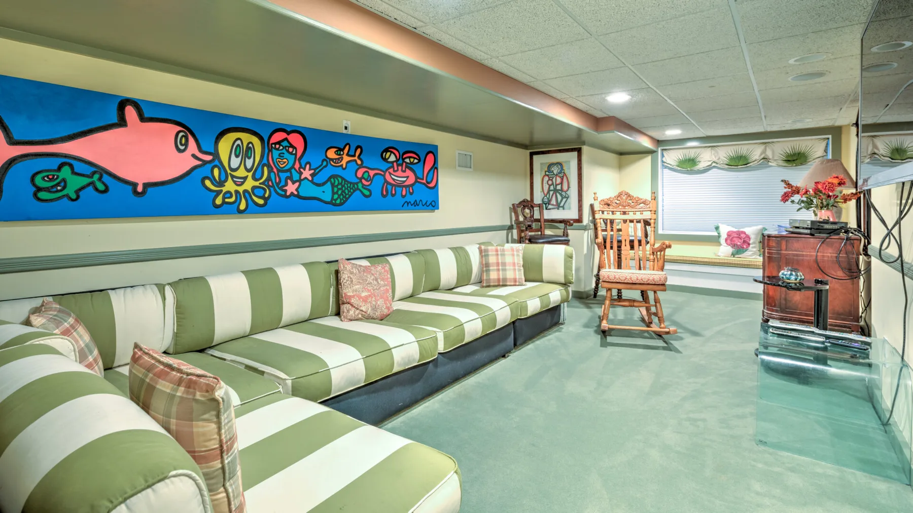 Una sala de estar en el sótano tiene asientos a rayas, una mecedora de madera y un mural colorido.