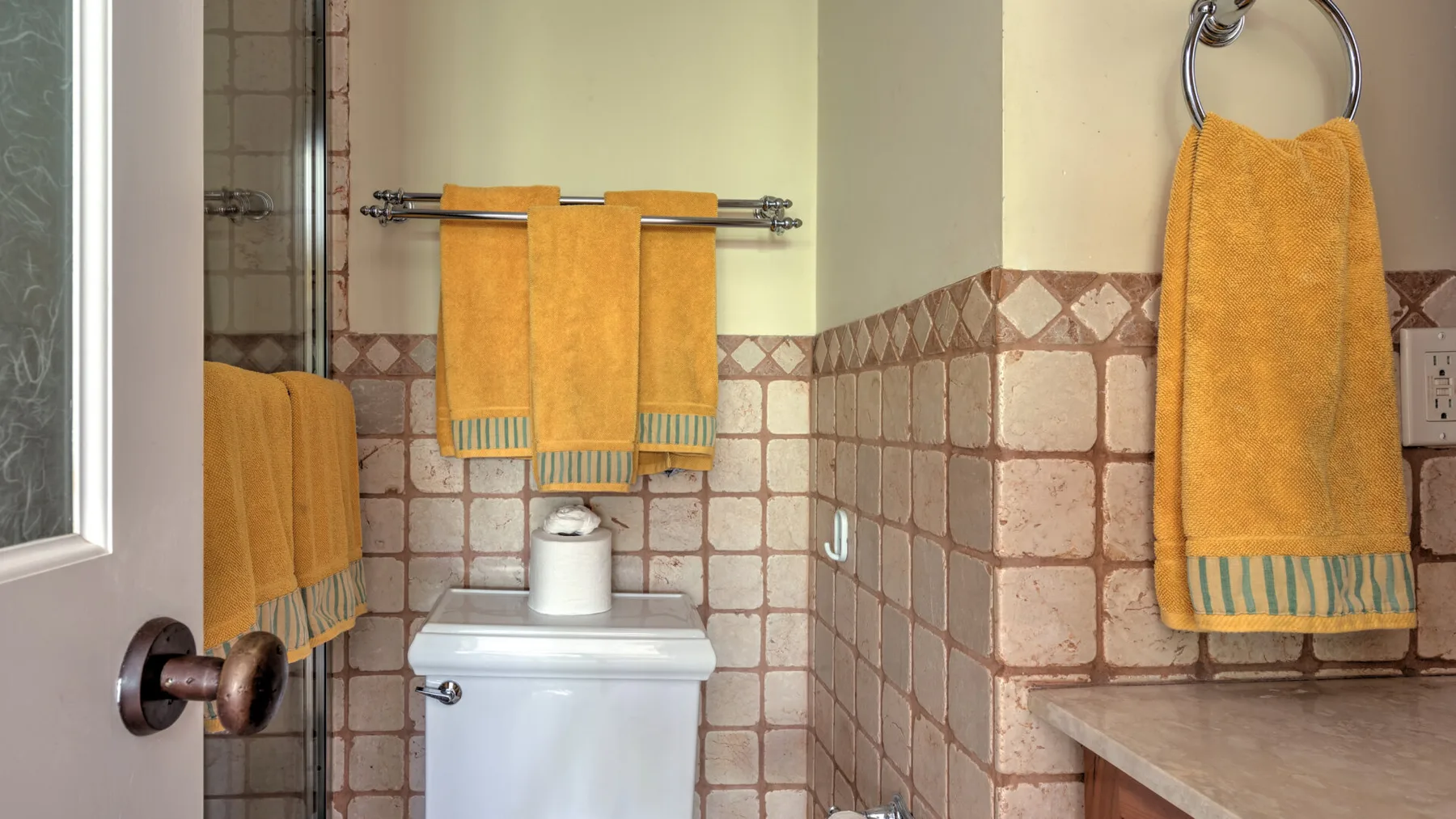 Un baño con un inodoro, paredes de azulejos y toallas naranjas.