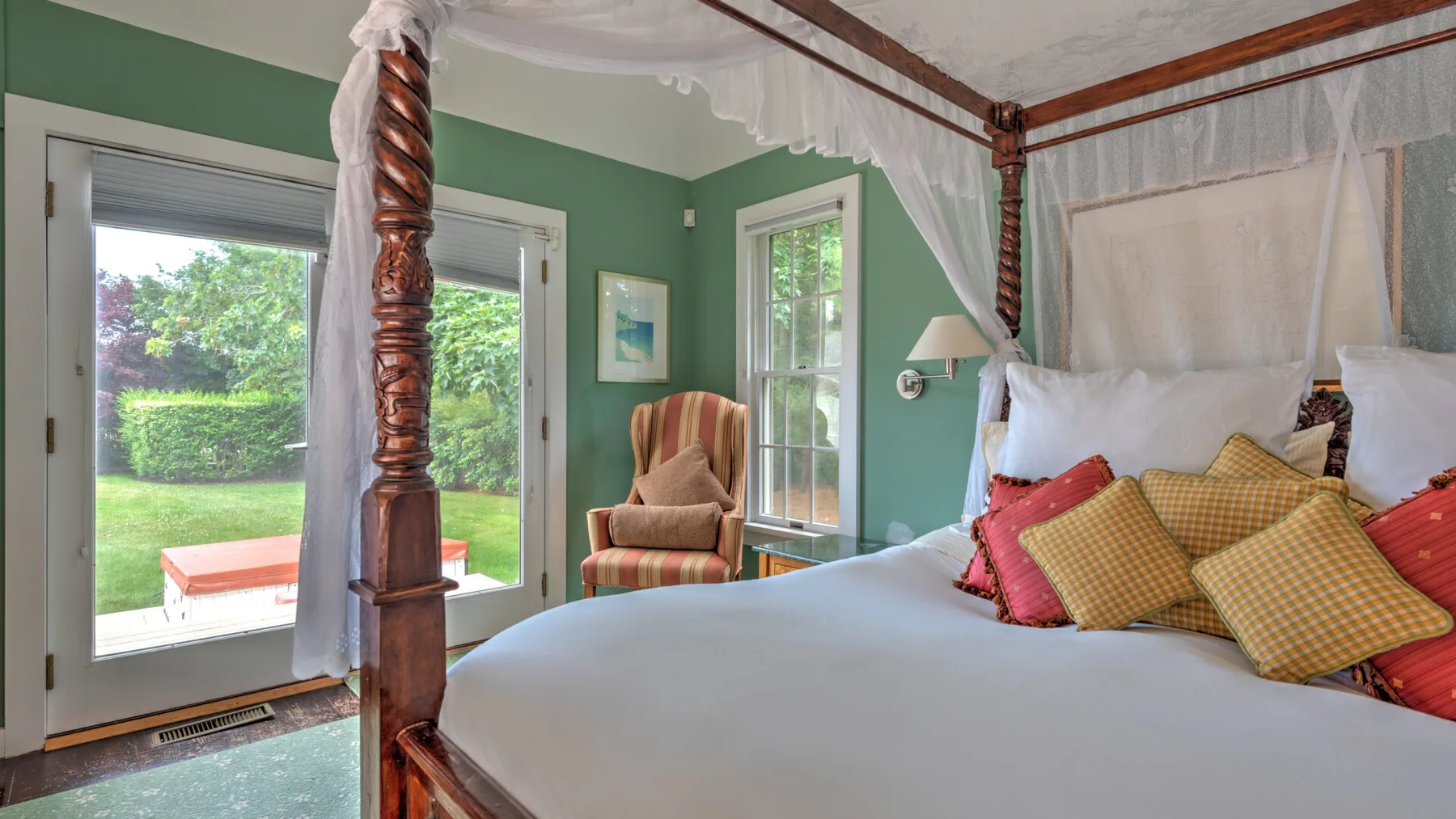 Un dormitorio con cama con dosel y ventanas con vistas a un jardín verde.