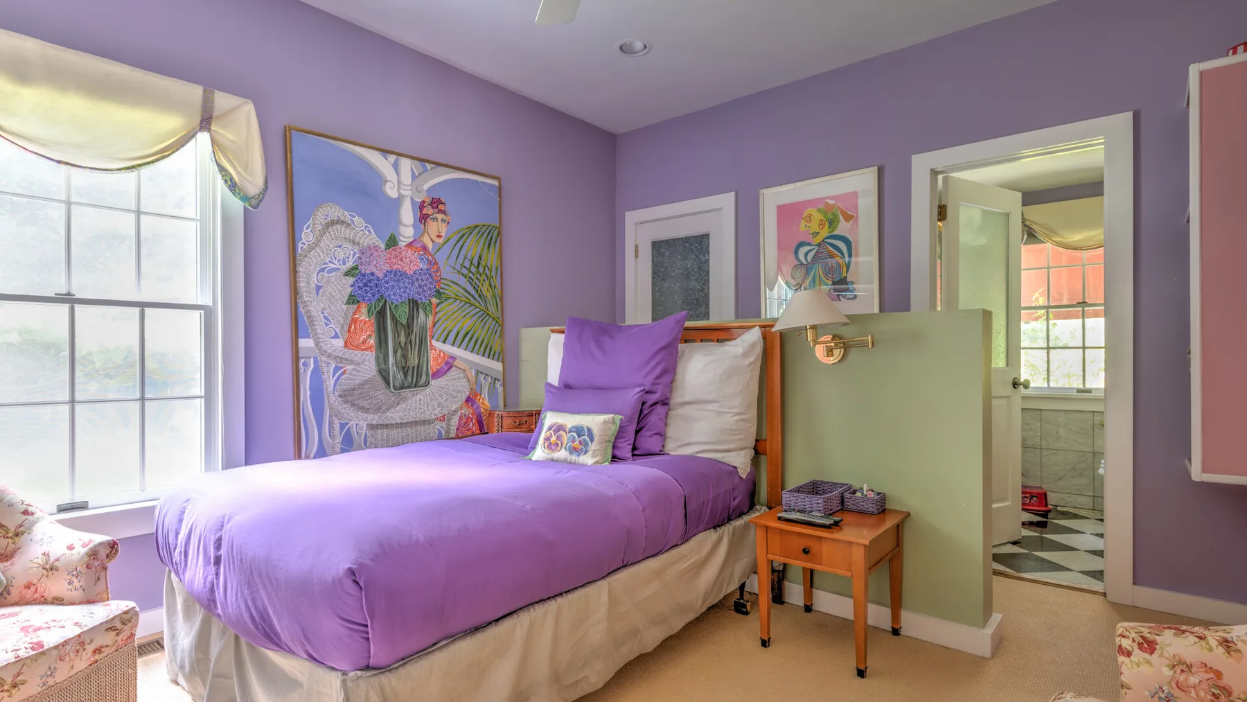 Un dormitorio con una cama morada, arte colorido en las paredes y una ventana.