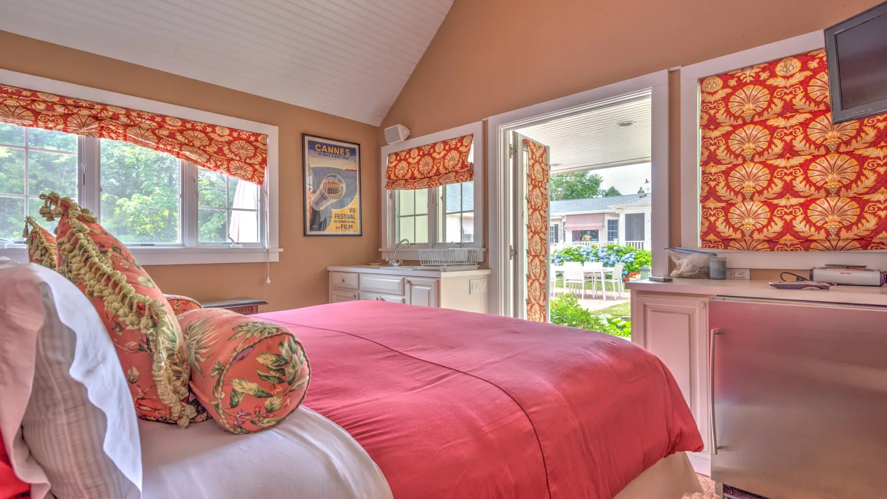 Un dormitorio con una cama cubierta con una colcha roja y cortinas florales coloridas.