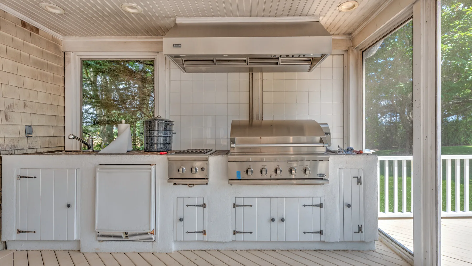 Una cocina exterior cubierta con una gran parrilla empotrada y gabinetes blancos.