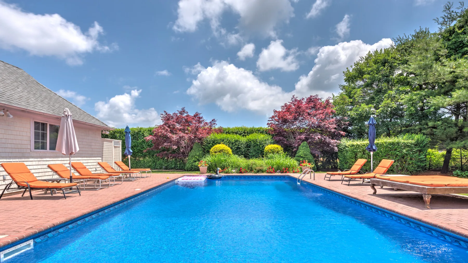 Una piscina al aire libre está rodeada por una terraza pavimentada y un jardín.