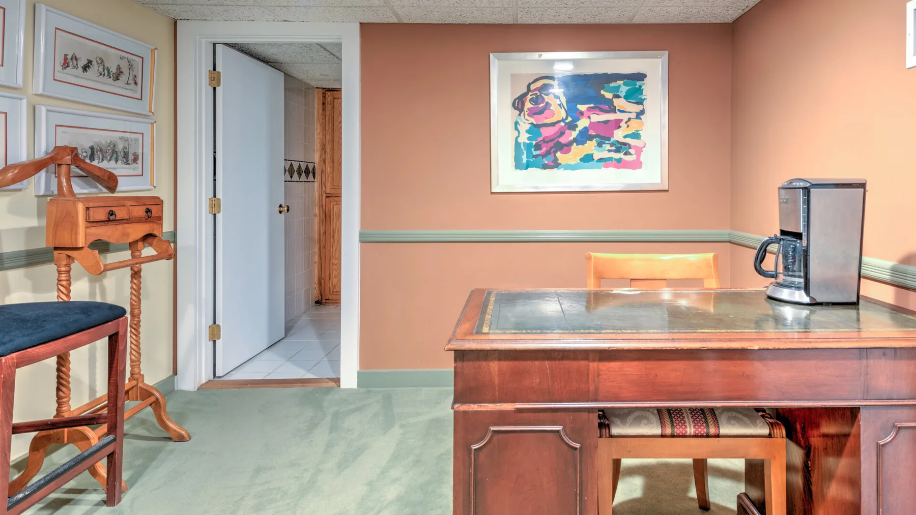 Una habitación amueblada con un escritorio de madera, asientos y obras de arte coloridas enmarcadas.