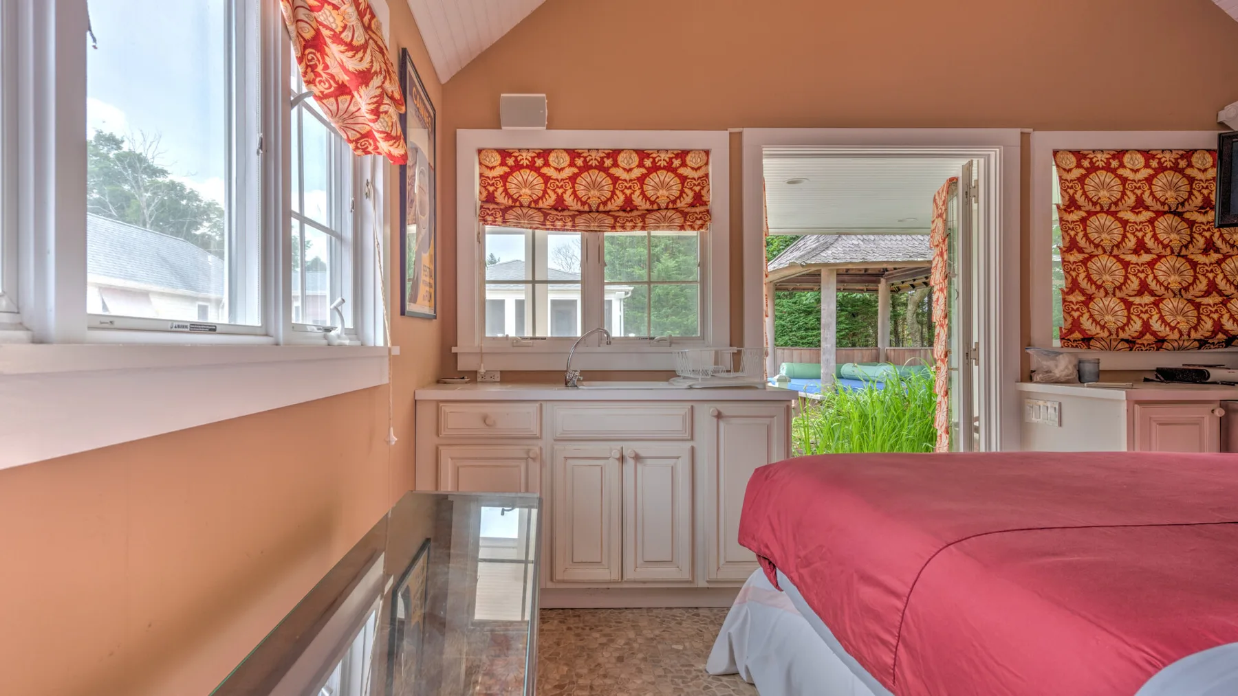 Un dormitorio con una cama rosa junto a un tocador luminoso y una puerta abierta.