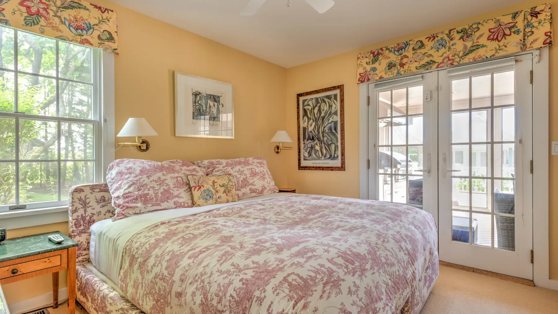 Un dormitorio con una cama cubierta con estampado floral y puertas con paneles de vidrio.