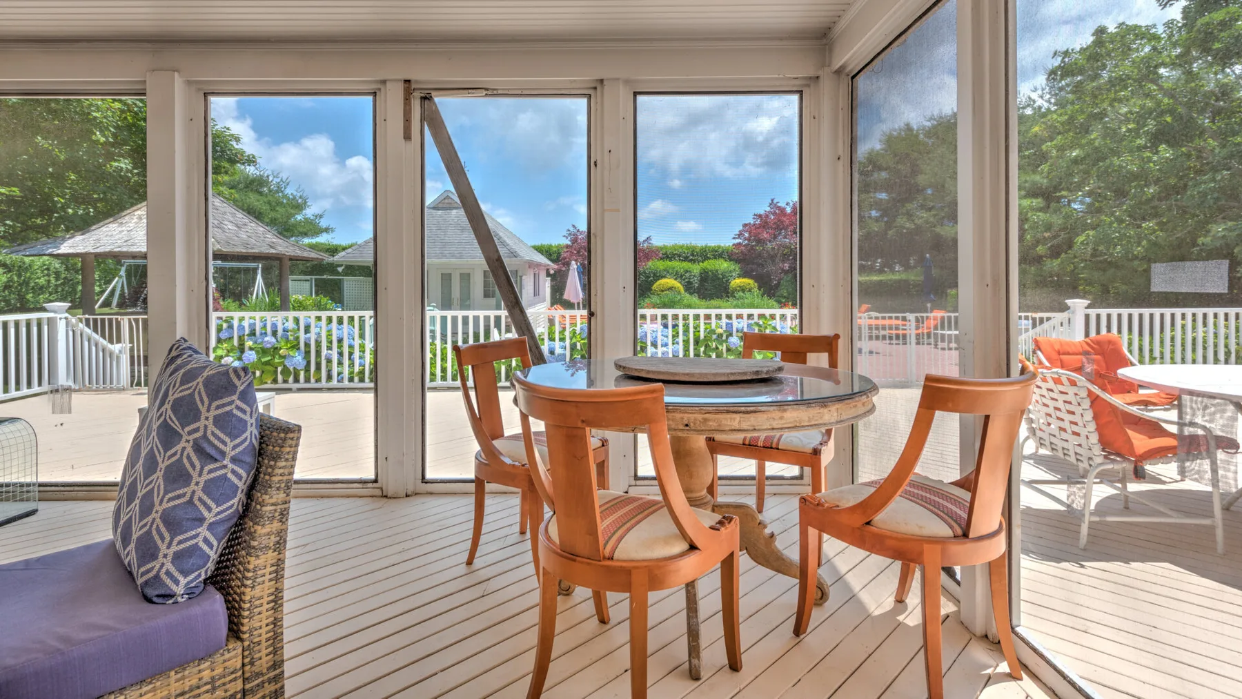 Un comedor acristalado da a una terraza, con una mesa de madera y sillas.