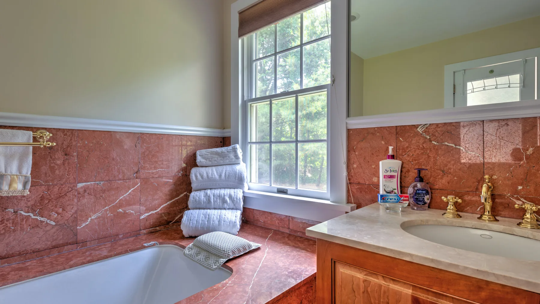 Un lavabo de baño y una bañera están bajo una ventana grande.