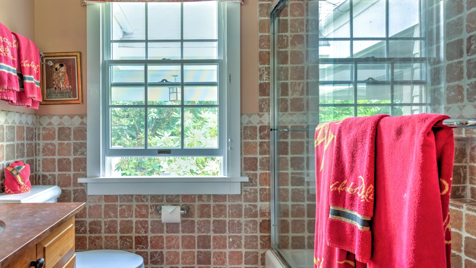 Un baño con azulejos tiene una ventana grande y toallas de color rosa brillante.