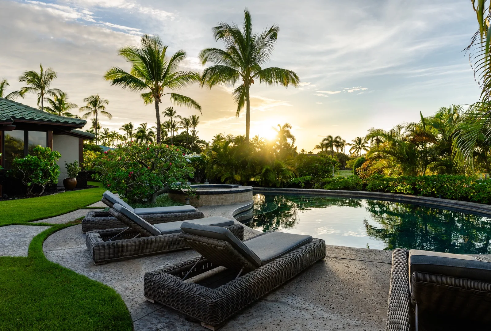 Una zona tropical junto a la piscina, con asientos y palmeras al atardecer.