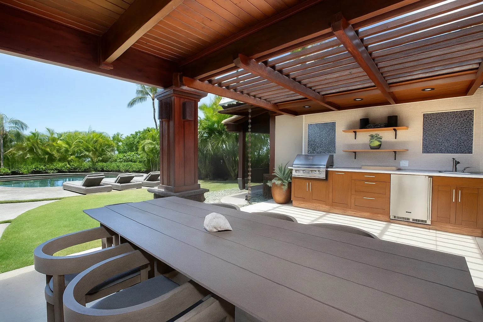 Comedor exterior cubierto junto a una piscina, con una cocina al aire libre.