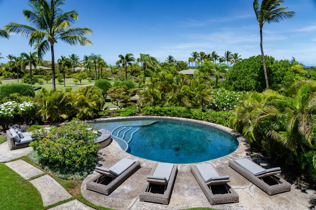 Una piscina curva está rodeada de vegetación tropical y asientos para descansar.
