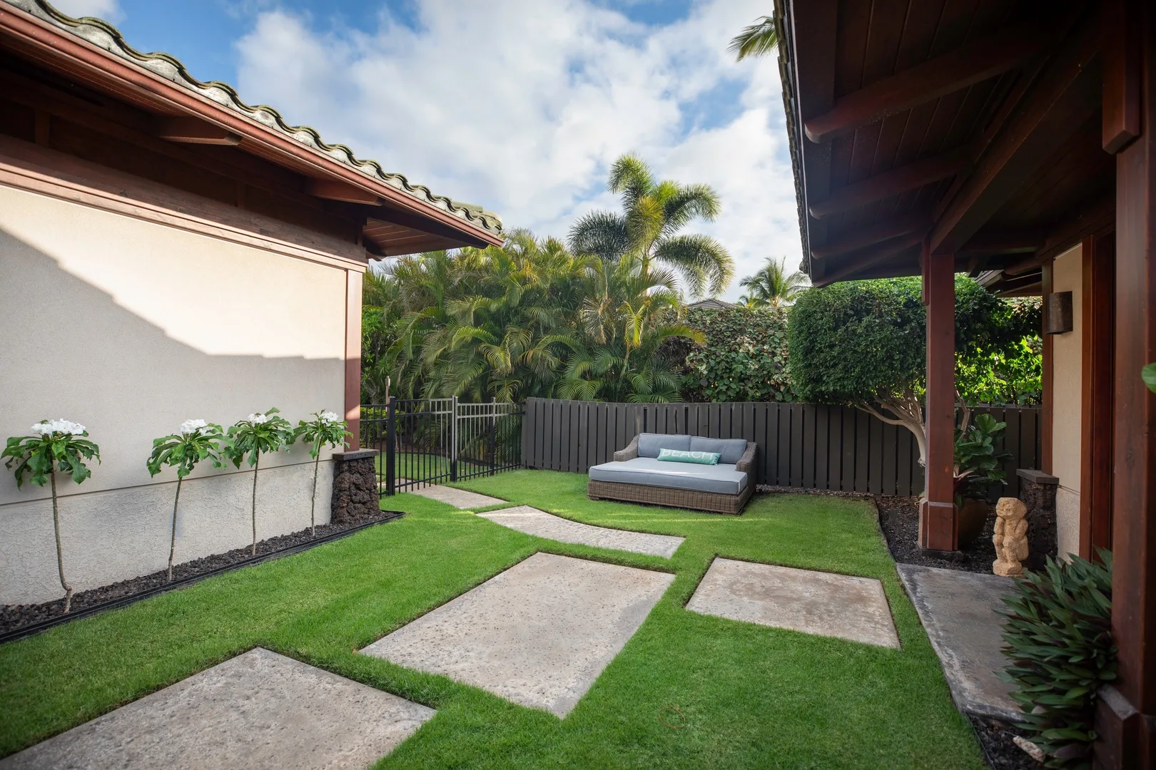 Un pequeño patio exterior con un sofá, caminos pavimentados y una cerca de jardín.