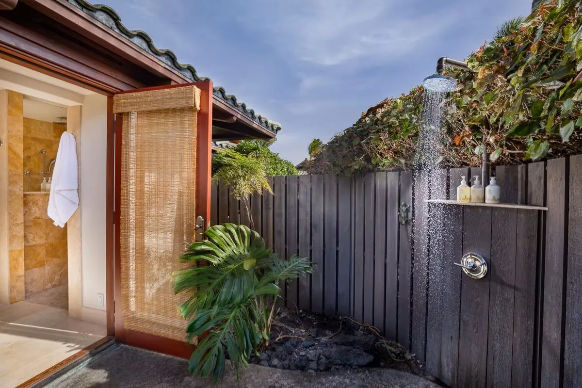 Una ducha exterior junto a una cerca de madera, con plantas tropicales cerca.