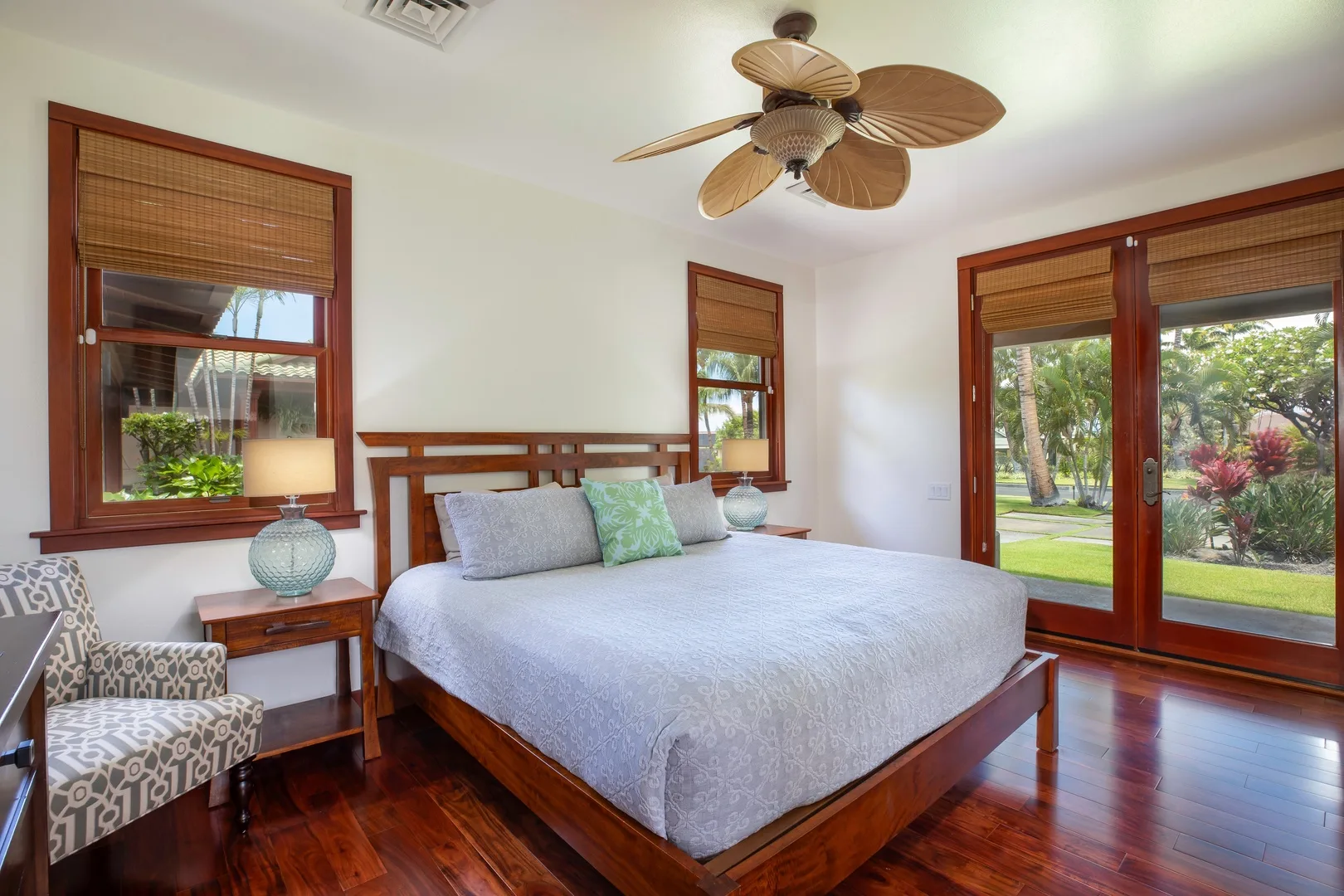 Un dormitorio con una cama grande, un sillón estampado y ventanas con vistas a la vegetación.