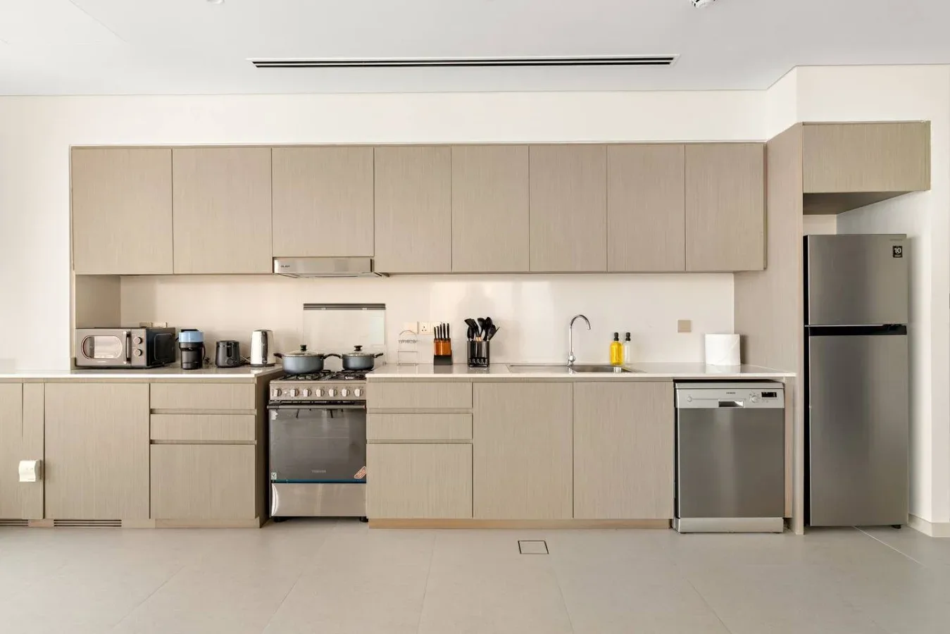 Una cocina moderna con armarios claros, placa de cocción, fregadero y electrodomésticos de acero inoxidable.