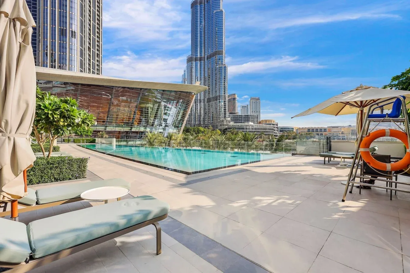 Una terraza con piscina, asientos para descansar y edificios altos al fondo.