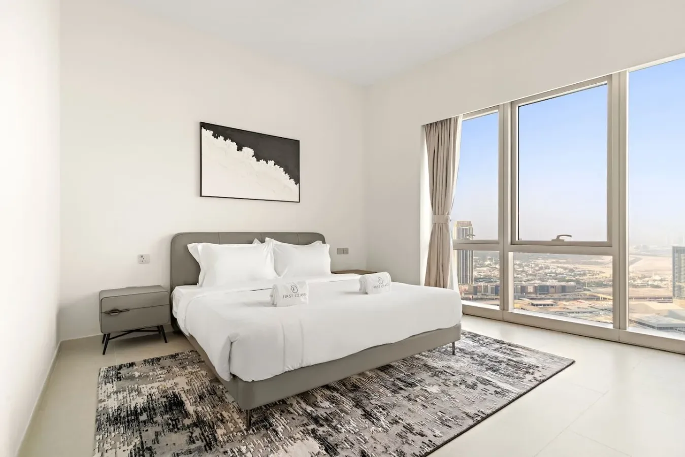 Un dormitorio luminoso con una cama junto a grandes ventanas con vistas a la ciudad.