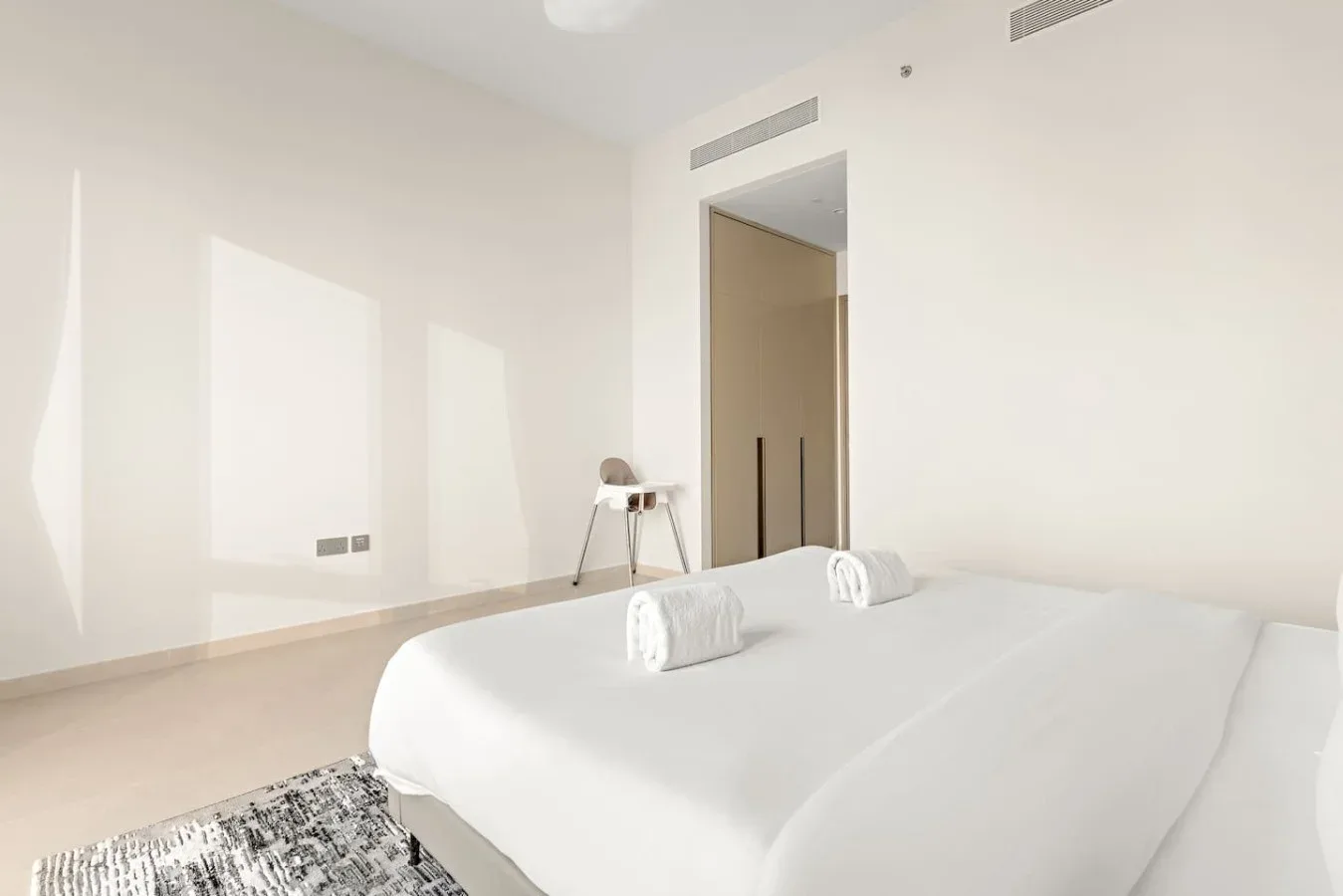 Un dormitorio luminoso con una cama tendida y dos toallas enrolladas.