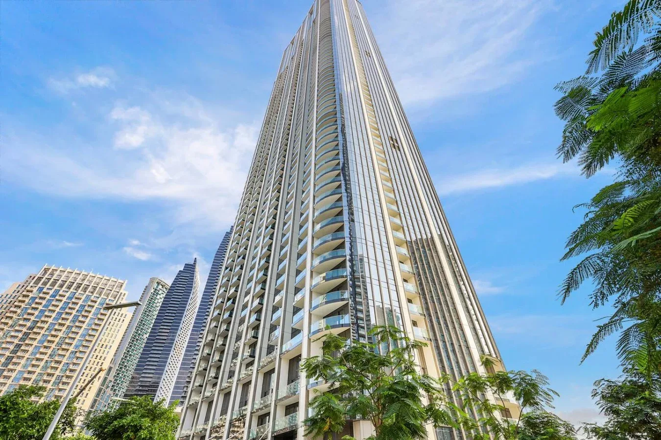 Un edificio alto se alza sobre los árboles cercanos bajo un cielo azul.