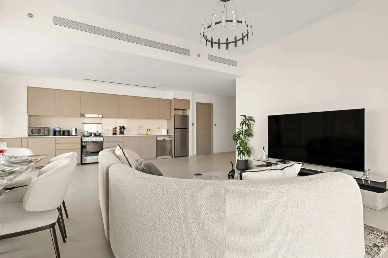 Sala de estar y cocina de concepto abierto, con un televisor grande y asientos claros.