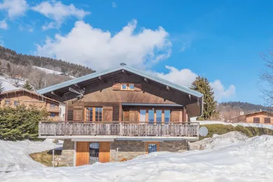 A chalet-style building with a broad balcony stands in a snowy mountain setting.