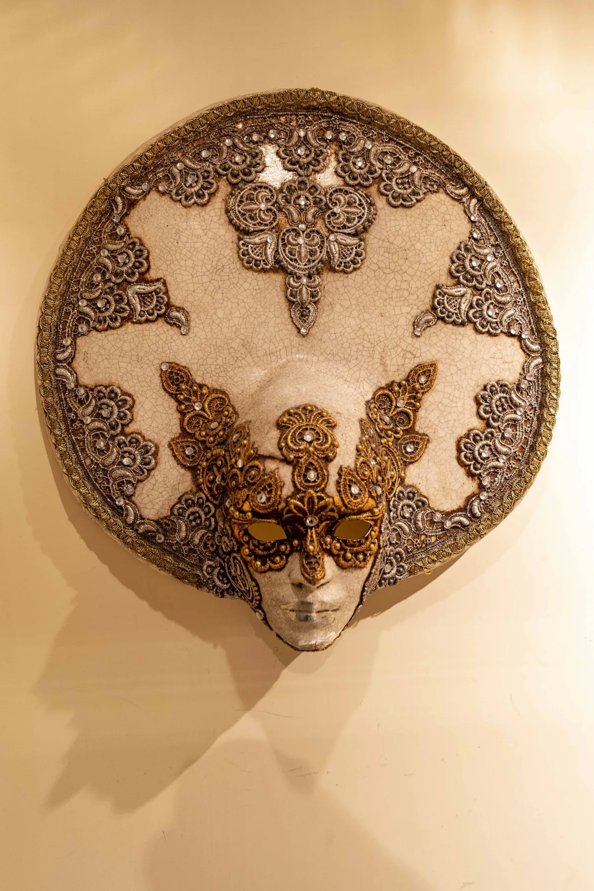 A decorative lace mask is displayed on a warmly lit wall.