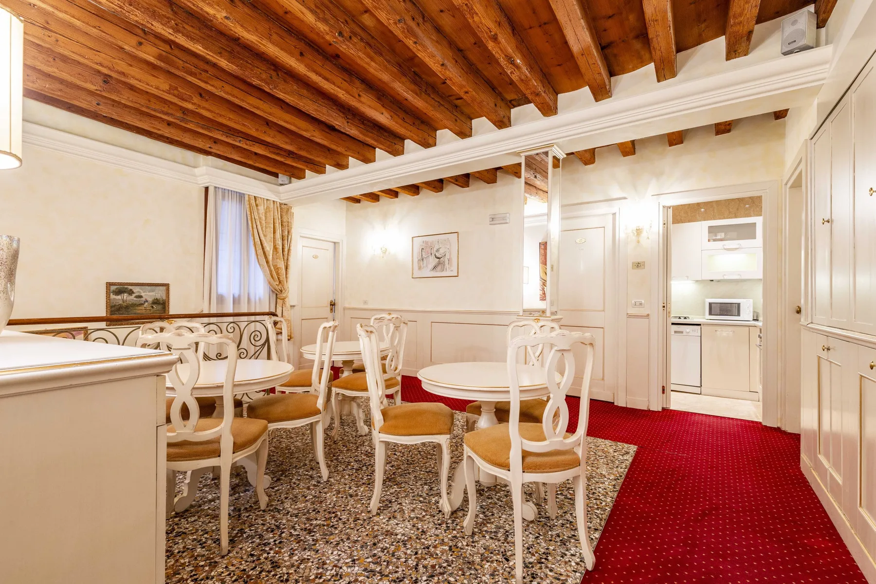 A dining room with a round table and white chairs beneath exposed wooden ceiling beams.
