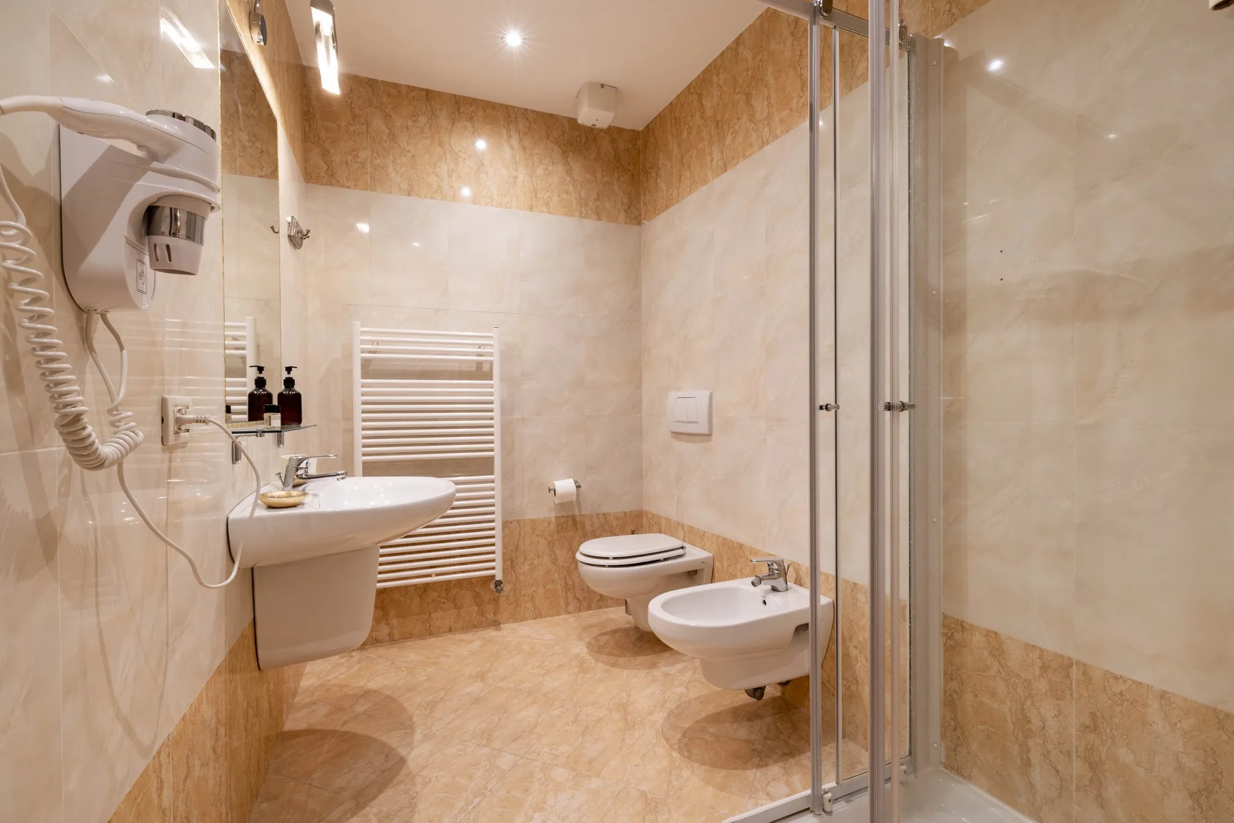 A tiled bathroom with a sink, toilet, bidet, and glass shower.
