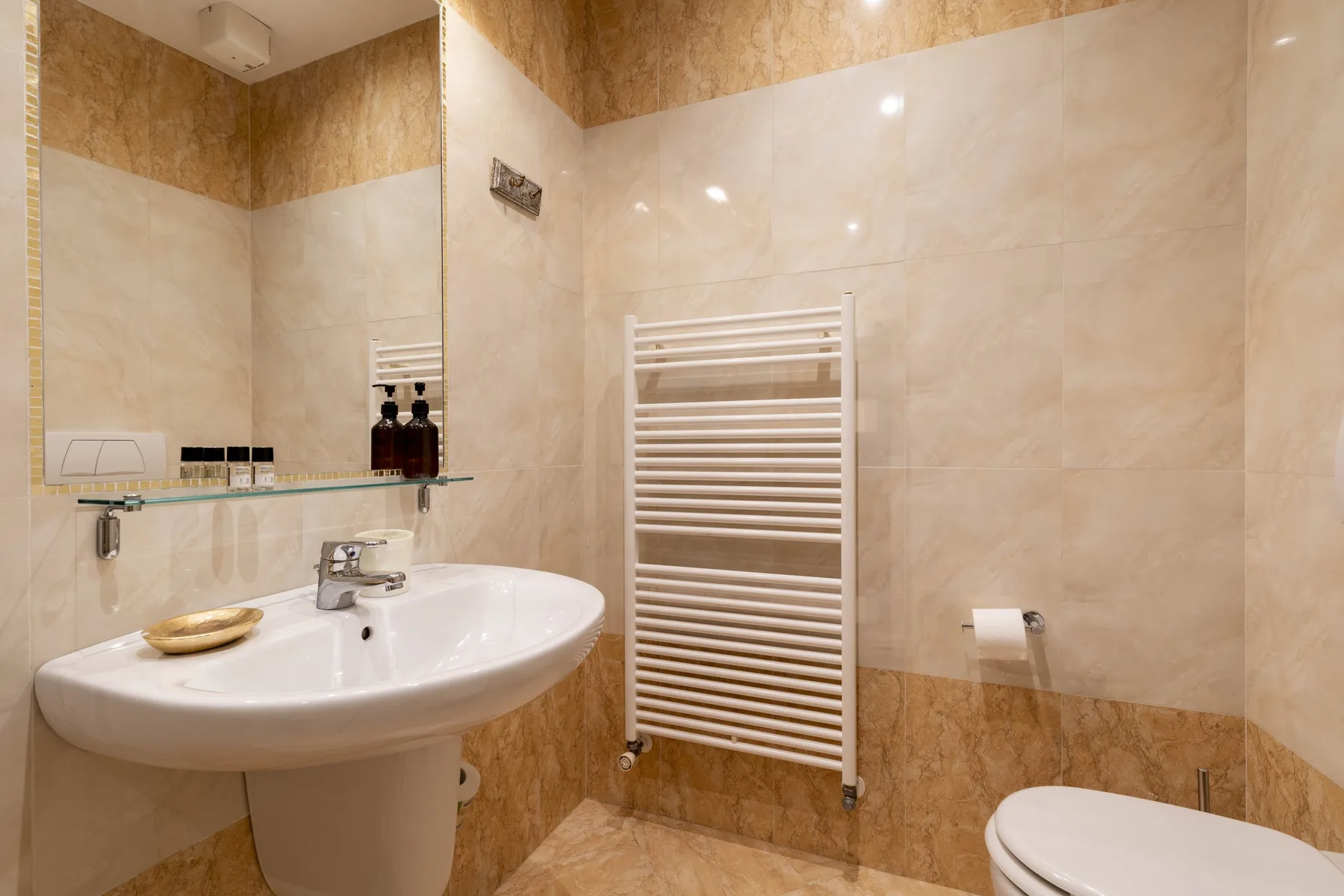 A tiled bathroom with a sink, towel radiator, and toilet.