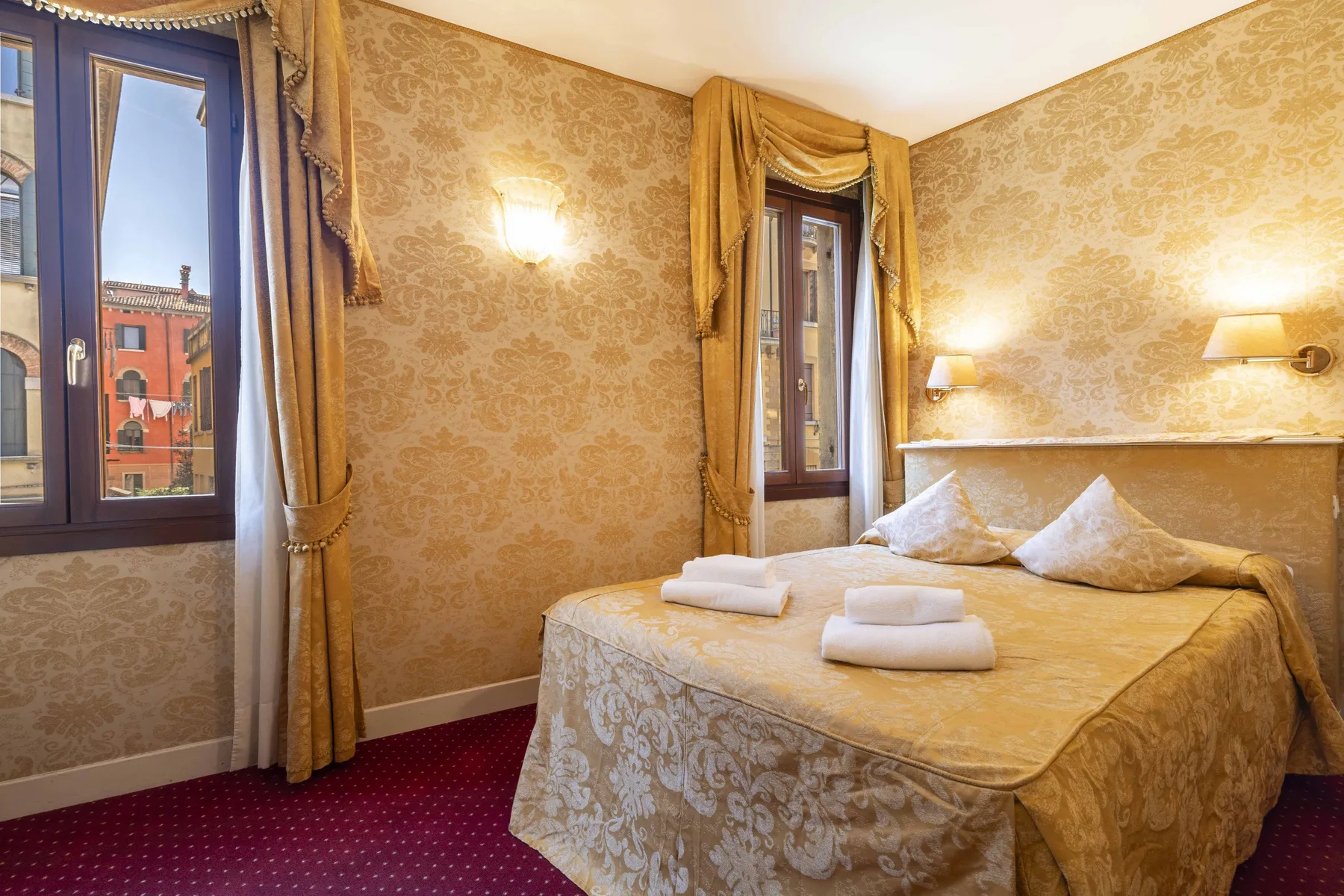 A bedroom with a double bed, decorative curtains, and two tall windows.
