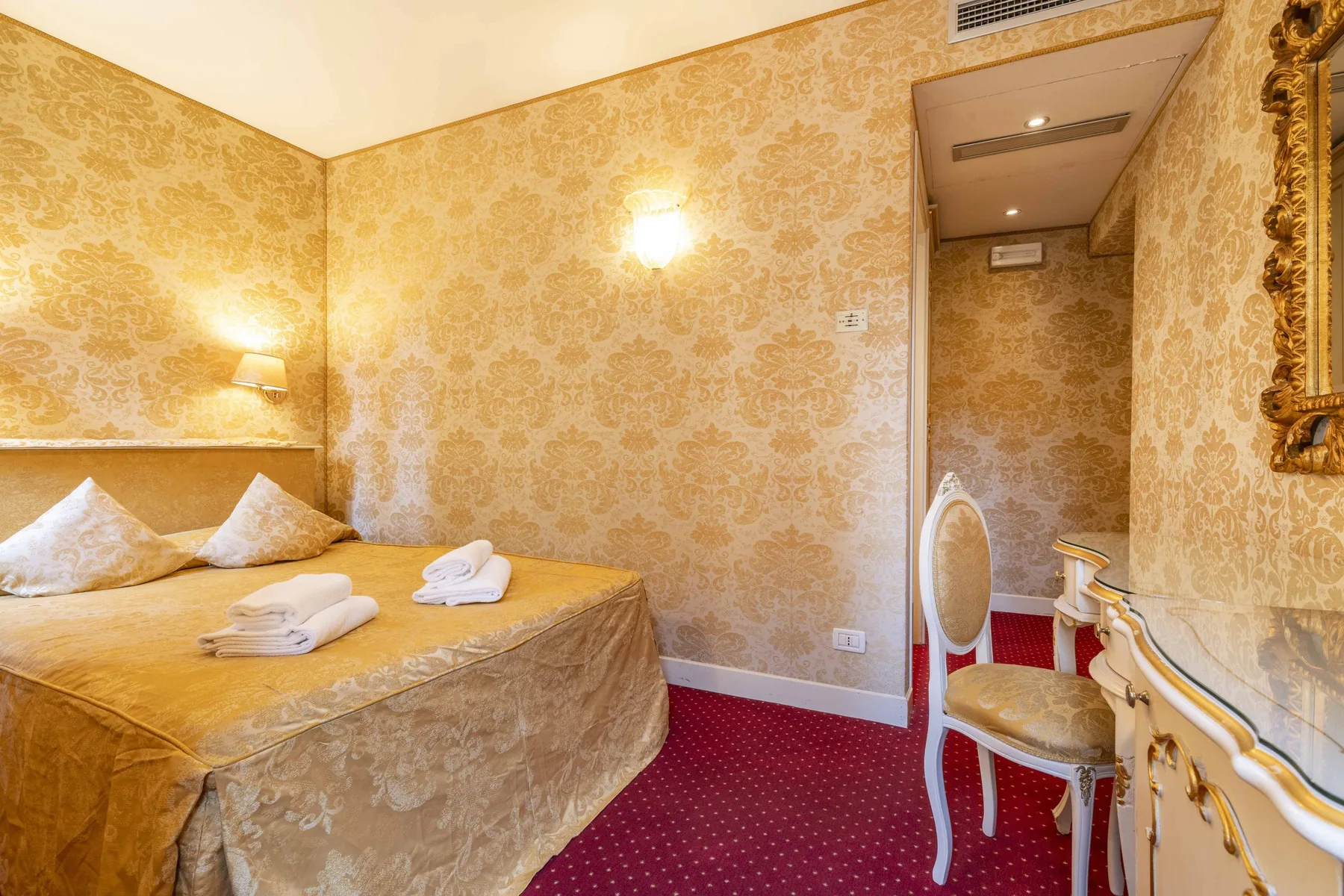 A bedroom with patterned gold walls, a bed, and a small seating area.