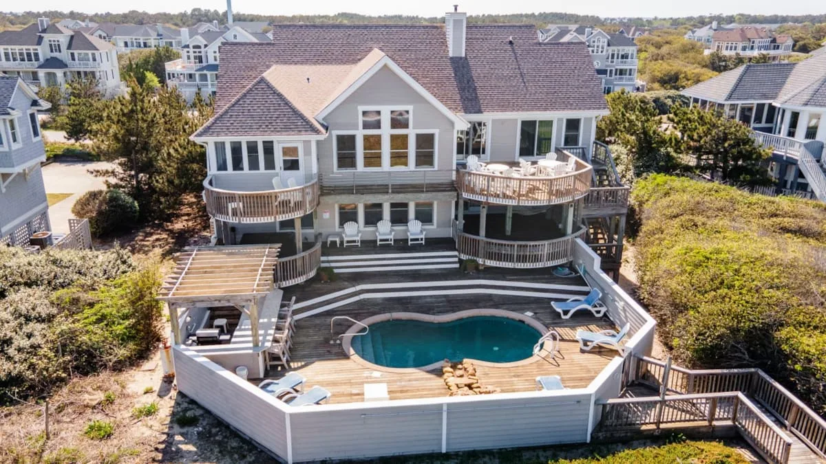 A large house overlooks a deck with a swimming pool and outdoor seating.