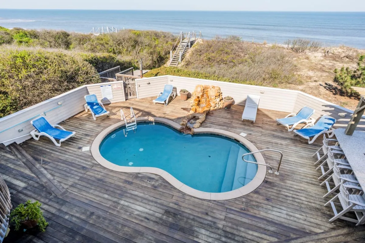 A swimming pool sits on a wooden deck overlooking the ocean.