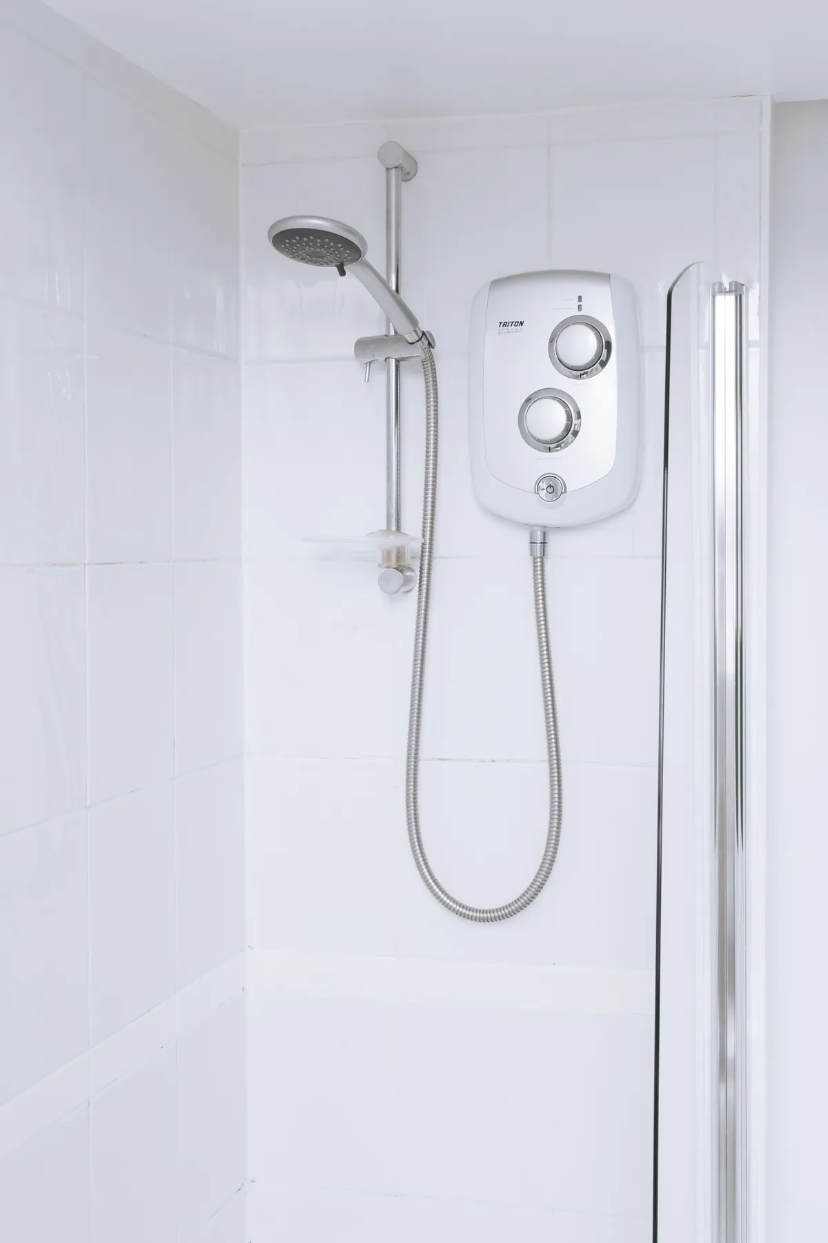 Una ducha con azulejos, cabezal de ducha y controles montados en la pared.