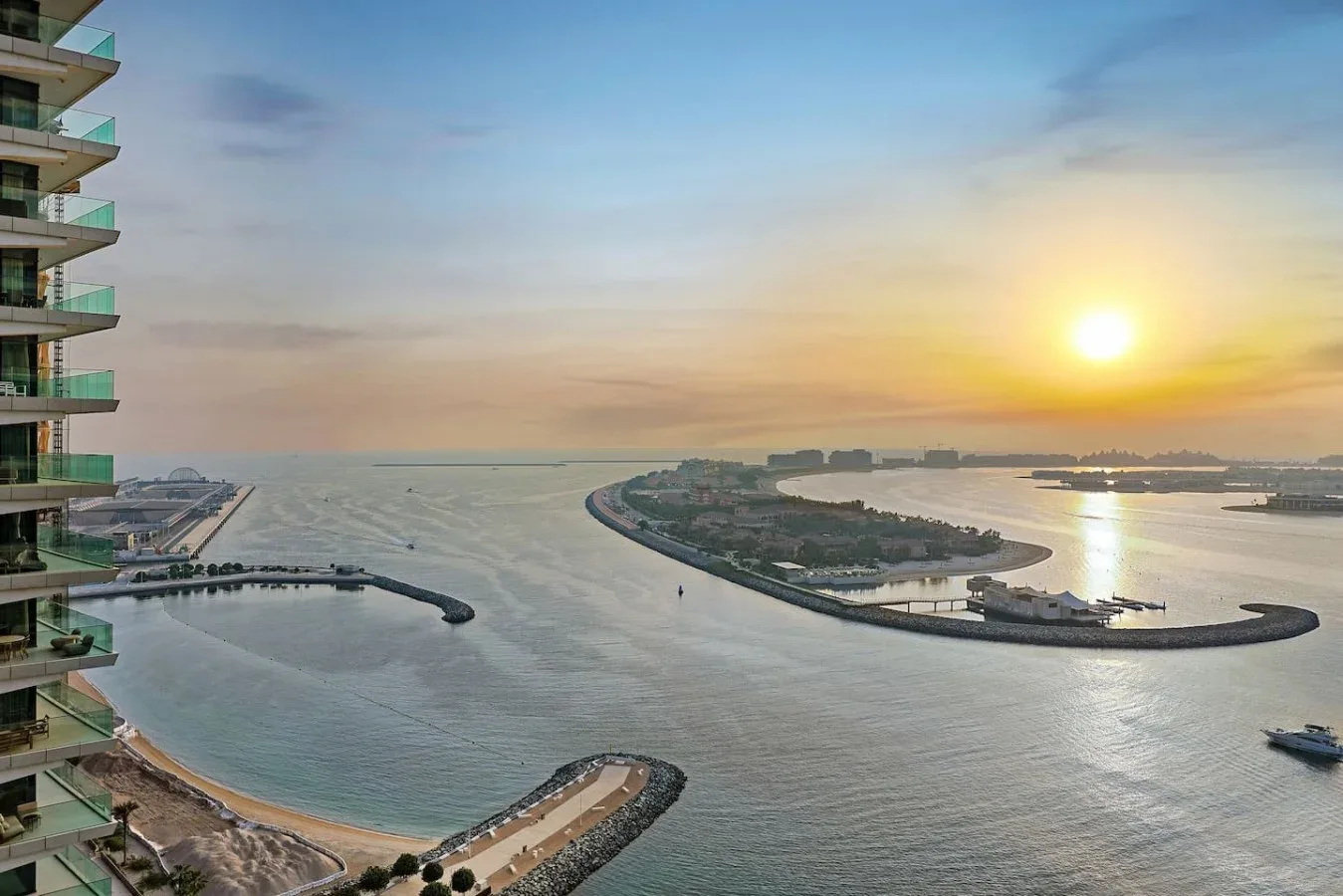 Atardecer sobre una costa, con una isla curva y edificios junto al agua.