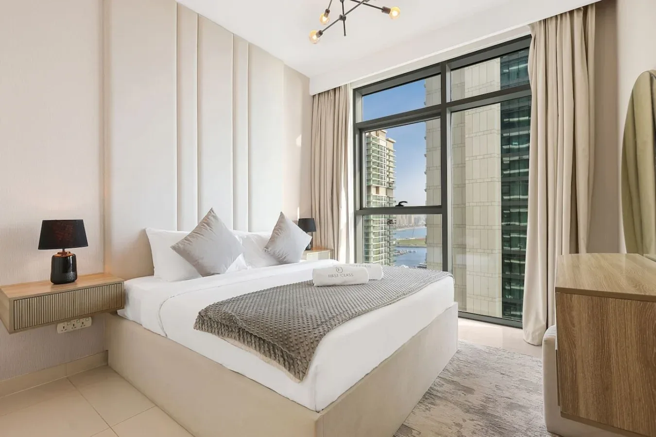 Un dormitorio luminoso con una cama bien tendida junto a grandes ventanas.