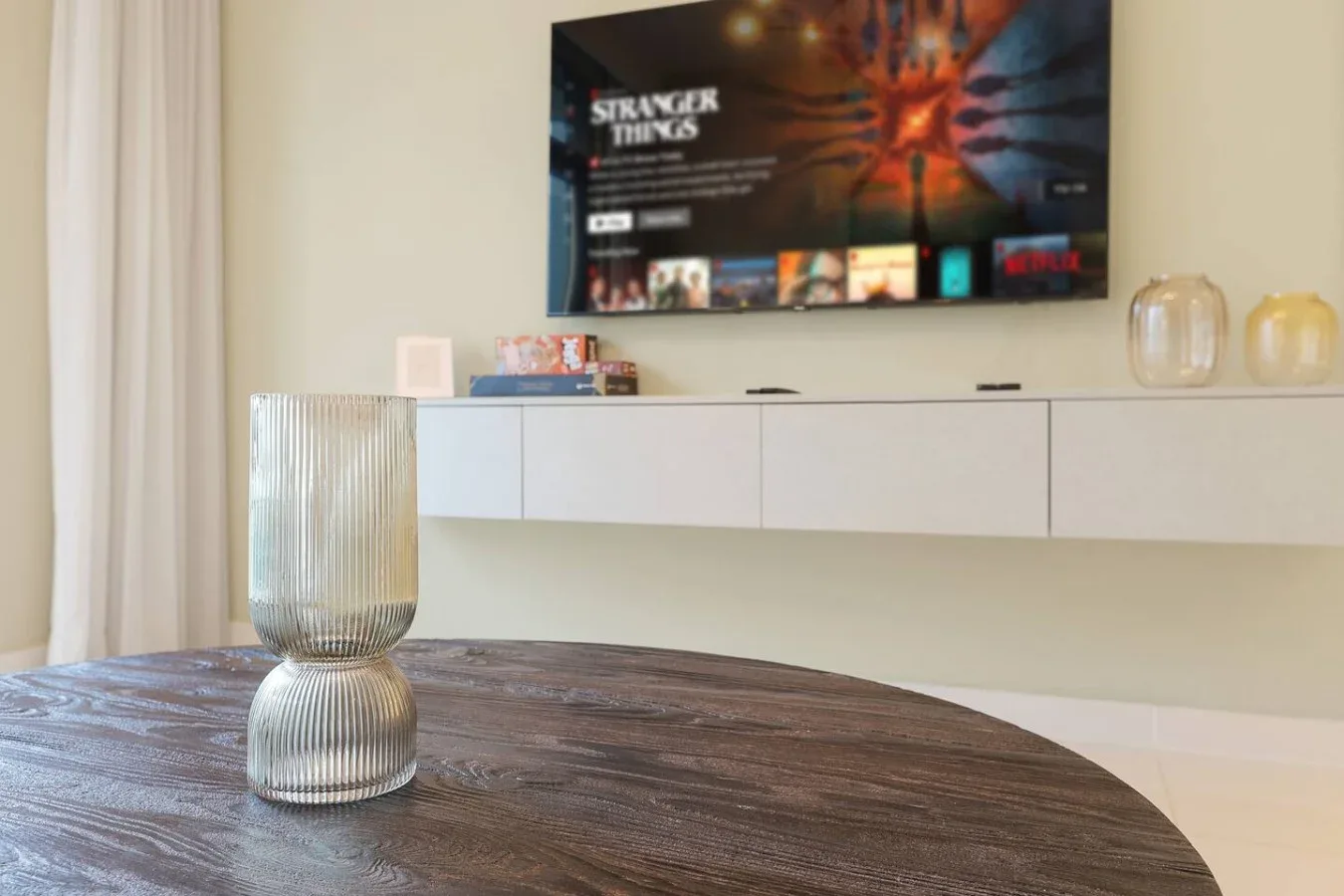 Una mesa de comedor con un jarrón decorativo de vidrio está debajo de un televisor montado en la pared.