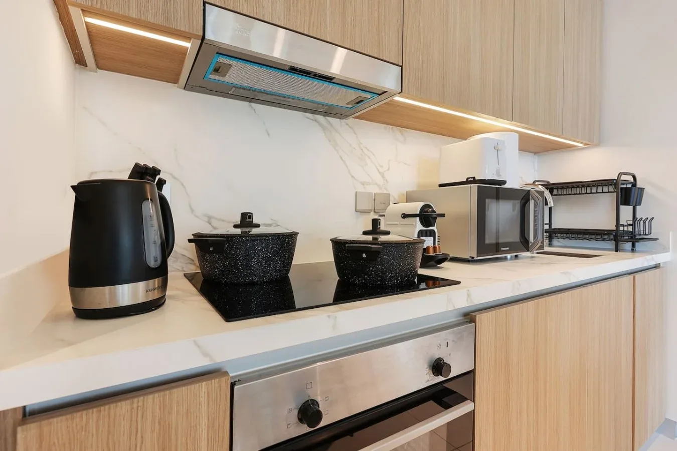 Una encimera de cocina moderna con placa de cocción, hervidor, microondas y escurridor.