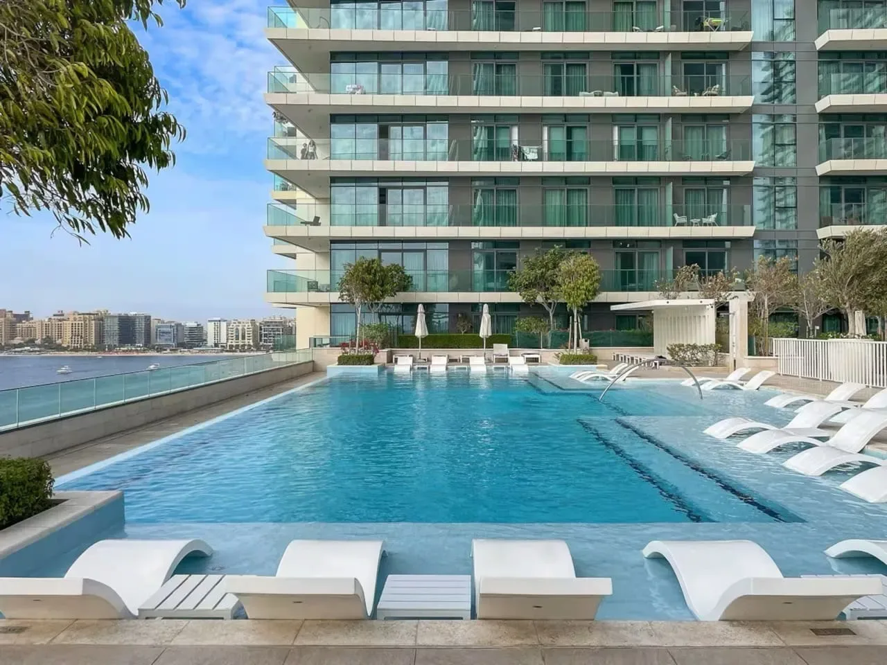 Una piscina al aire libre junto a un edificio moderno de gran altura, con asientos junto al agua.