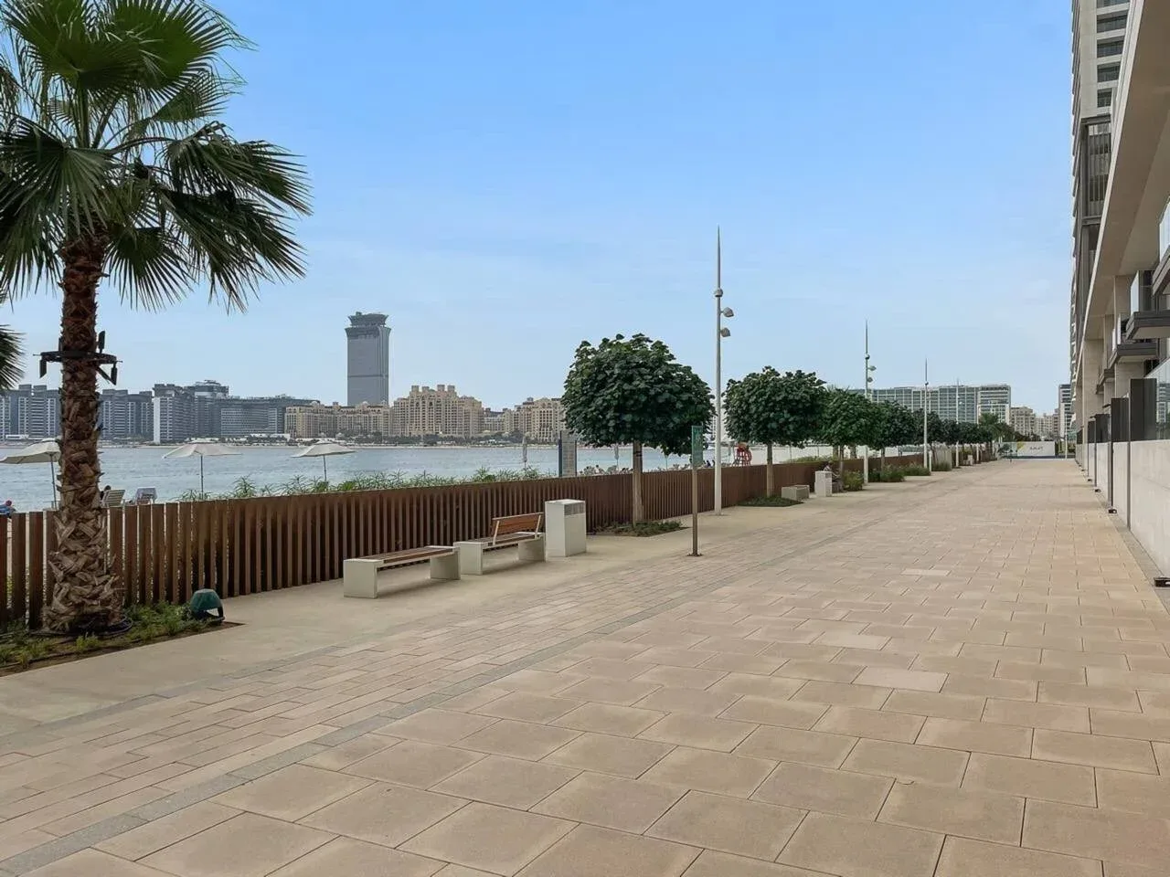 Un paseo pavimentado junto al río tiene árboles y bancos a lo largo del camino.